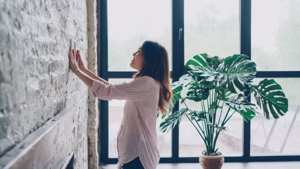 Personne qui règle un thermostat connecté au mur